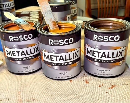 Open cans of Rosco Metallix Gilders Gold, Pyrate Gold, and Burnished Bronze paints.