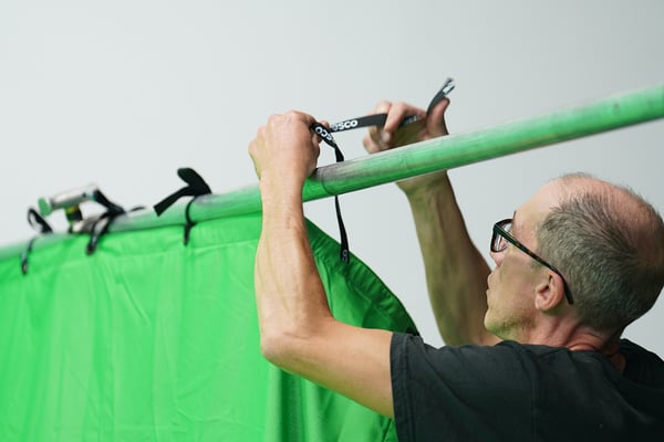Man tying a Rosco ChromaDrop green backdrop onto a truss.