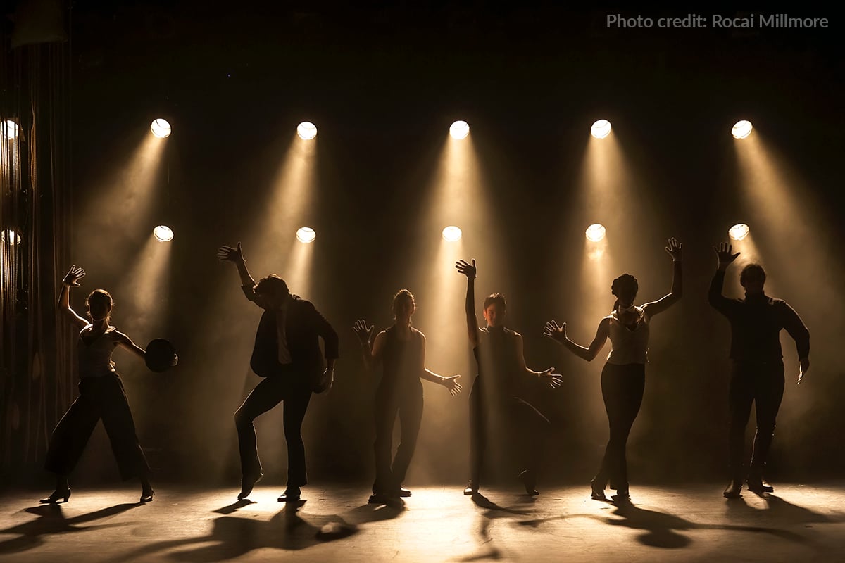 Dancers on the stage are backlit with un-colored light from warm, tungsten lights. 