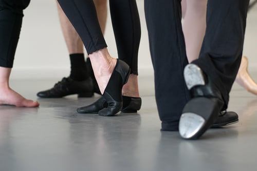 People wearing a range of dance shoes on a dance floor.