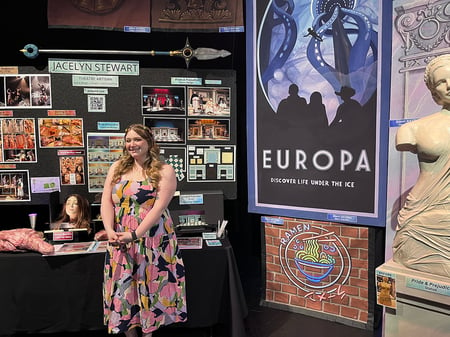 Photo of Scenic Artist Jacelyn Stewart.  posing with her Neon scenery project that she painted with Rosco Fluorescent Paint.