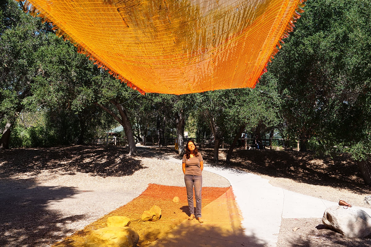 A woman standing underneath a woven gel textile experiences a sunset lighting effect.